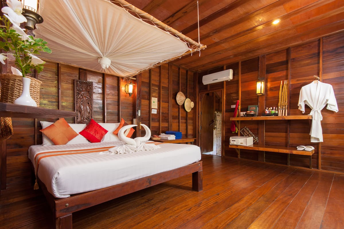 A wooden room with a bed, a hanging fan, a shelf with towels, and a wall-mounted air conditioner.