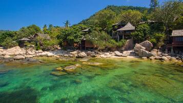 A coastal resort with clear waters, rocky shoreline, and traditional wooden buildings.