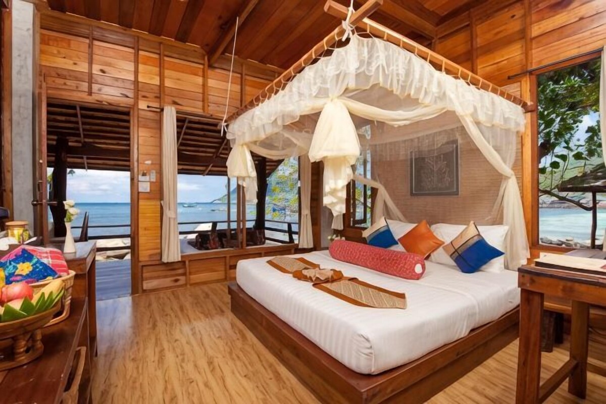 A wooden room with a bed, a table, and a view of the sea.