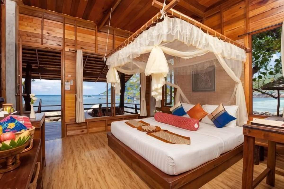 A wooden room with a bed, a table, and a view of the sea.