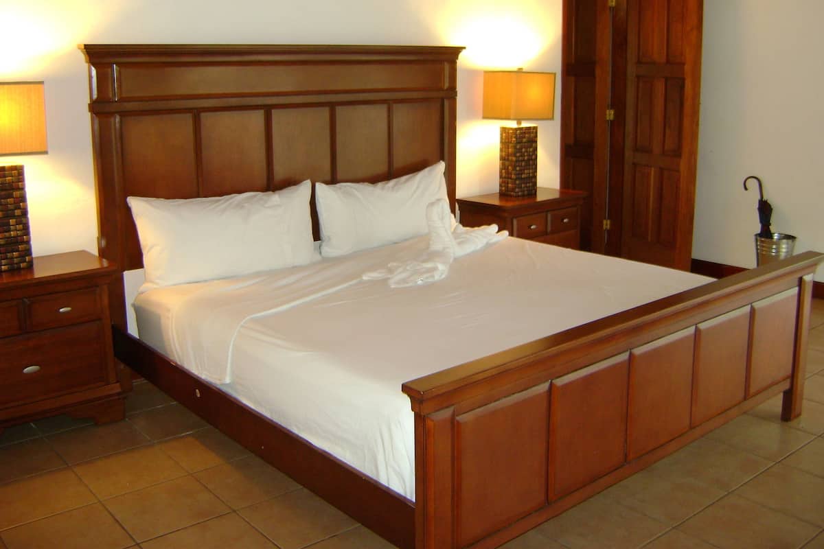 A large wooden bed with white linens, two bedside tables with lamps, and a wooden wardrobe.