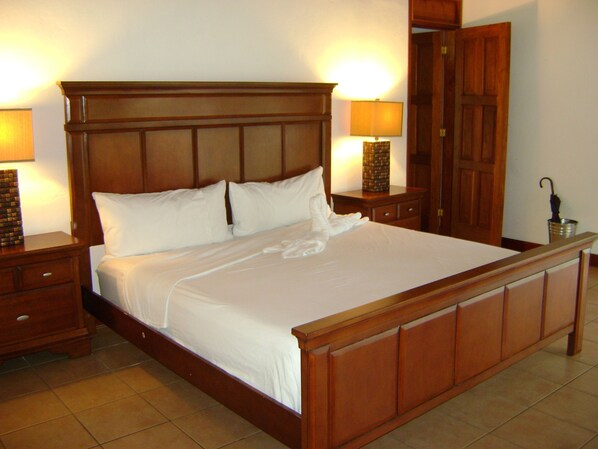 A large wooden bed with white linens, two bedside tables with lamps, and a wooden wardrobe.