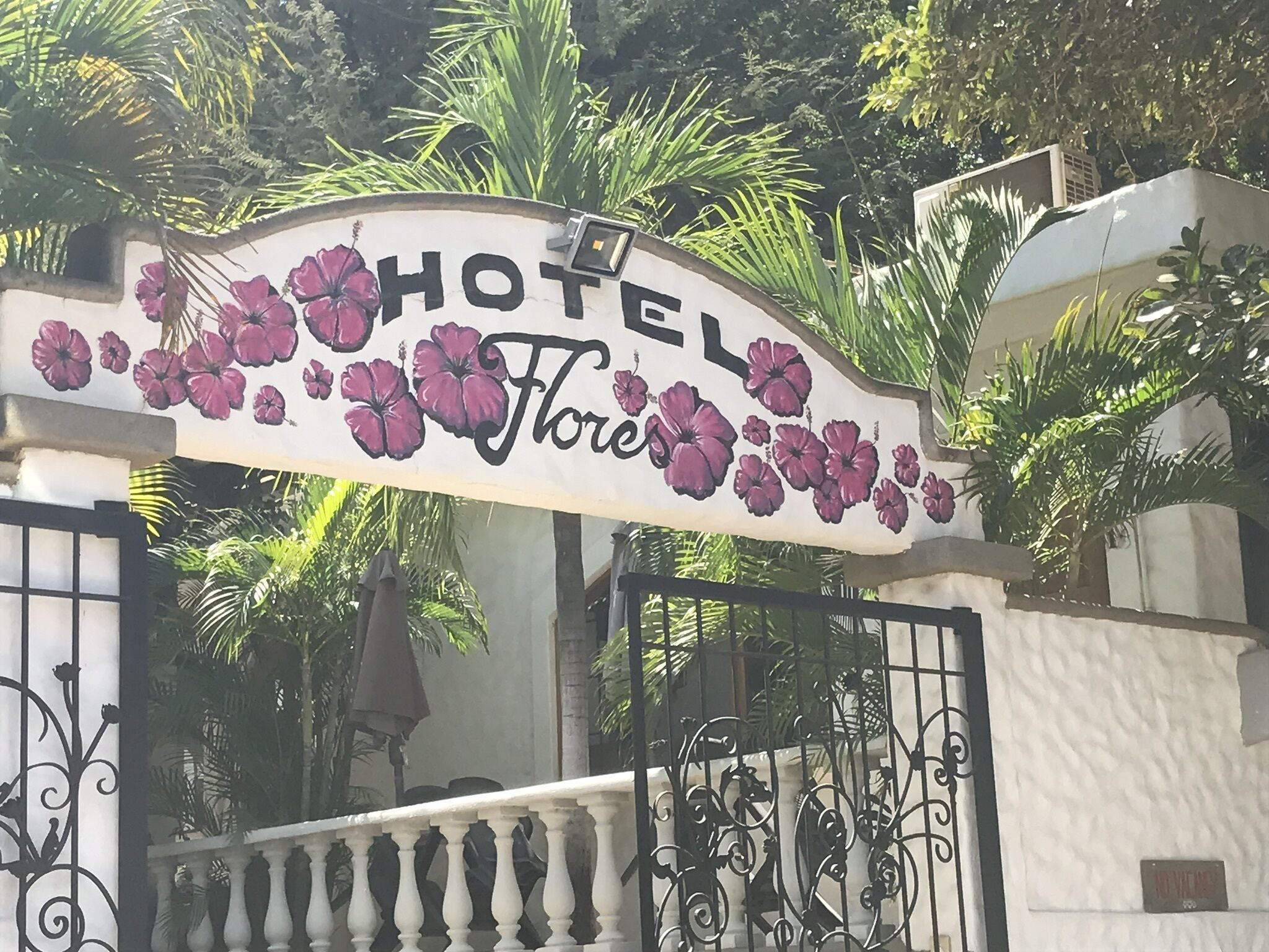 A hotel entrance with a sign that reads "HOTEL Floris" surrounded by lush greenery.