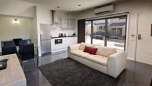 Una sala de estar moderna con sofá, mesa de comedor y zona de cocina al fondo.