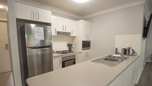 Una cocina moderna con gabinetes blancos, un refrigerador de acero inoxidable, un microondas, una estufa a gas y un lavamanos.