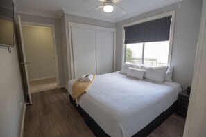 Une chambre avec un grand lit, un ventilateur de plafond, une fenêtre avec un store et une porte.