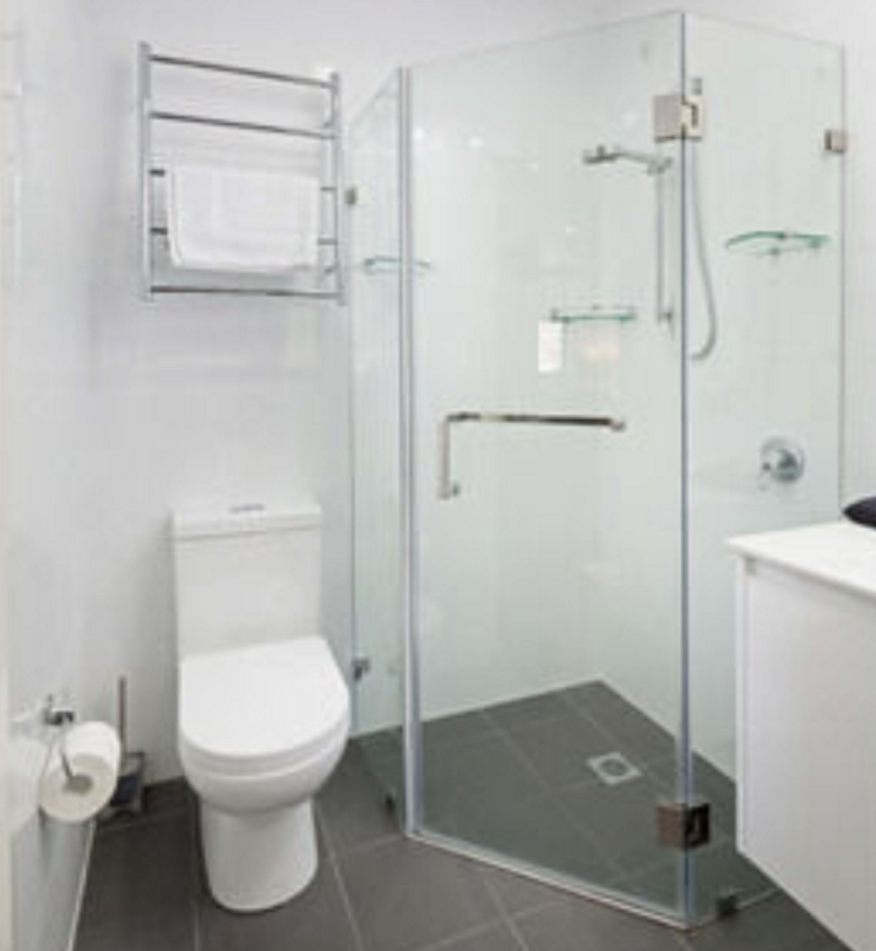 Un bagno moderno con doccia a vetro, un WC bianco e uno scaffale in vetro sopra il lavandino.