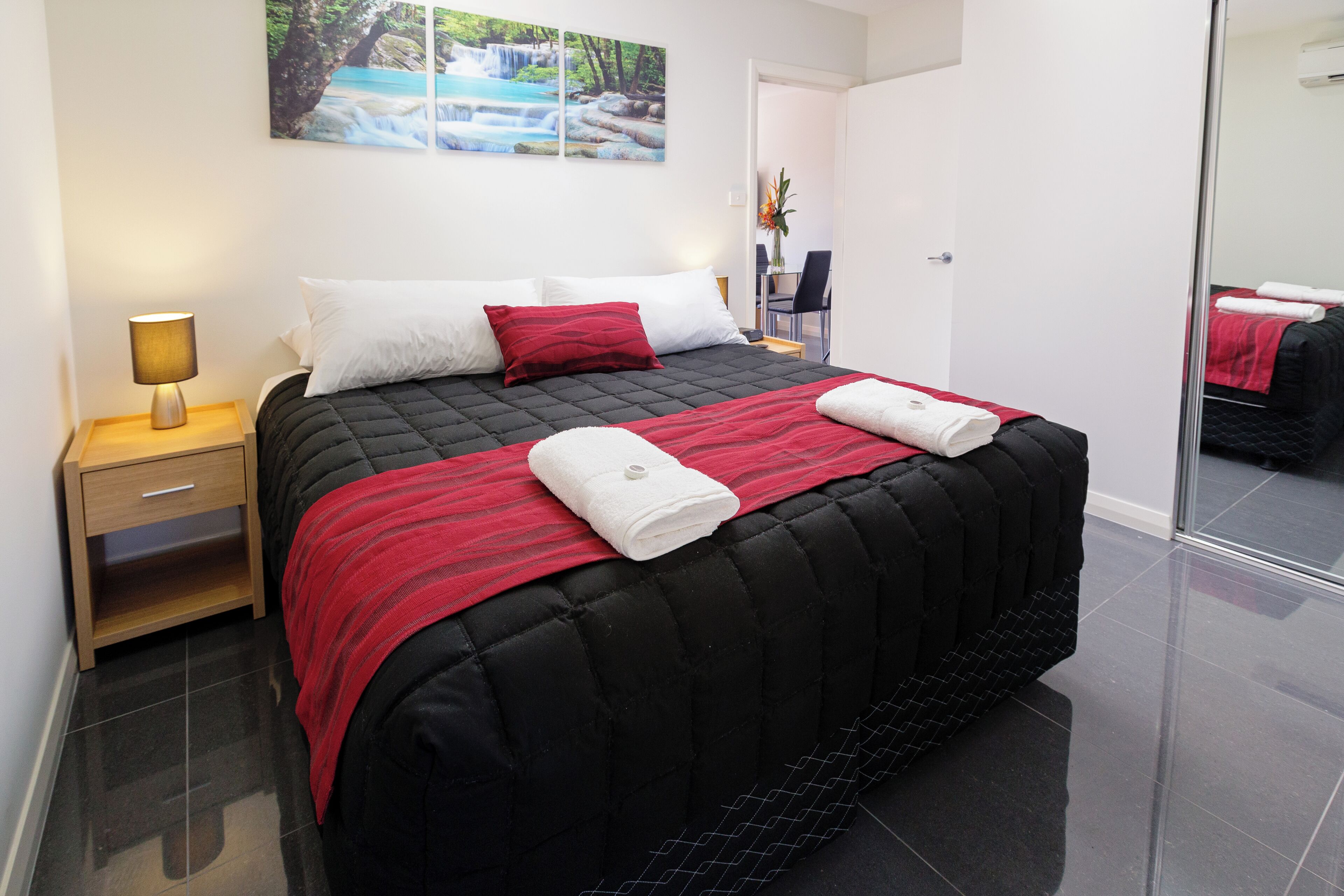 A modern hotel room with a large bed, a bedside table with a lamp, a chair, and a desk.