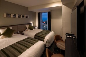 A hotel room with two beds, a desk, a chair, a TV, and a window with a city view.