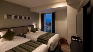 Quarto de hotel com duas camas, uma televisão, uma escrivaninha e vista para a cidade.