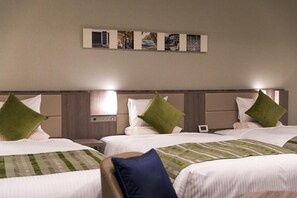 A hotel room with two beds, each with a green pillow, a bedside table, and a wall-mounted clock.