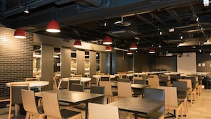 A spacious indoor area with multiple tables and chairs, red pendant lighting, and exposed ductwork on the ceiling. - Hotel Mystays Nagoya Nishiki (Nagoya)