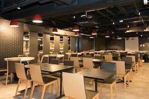 A spacious indoor area with multiple tables and chairs, red pendant lighting, and exposed ductwork on the ceiling.