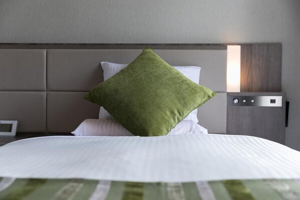 A neatly made bed with a green pillow, a white pillow, and a white duvet. - Hotel Mystays Nagoya Nishiki (Nagoya)