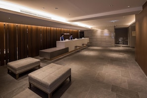 A hotel reception area with a reception desk, two receptionists, and a seating area with ottomans.