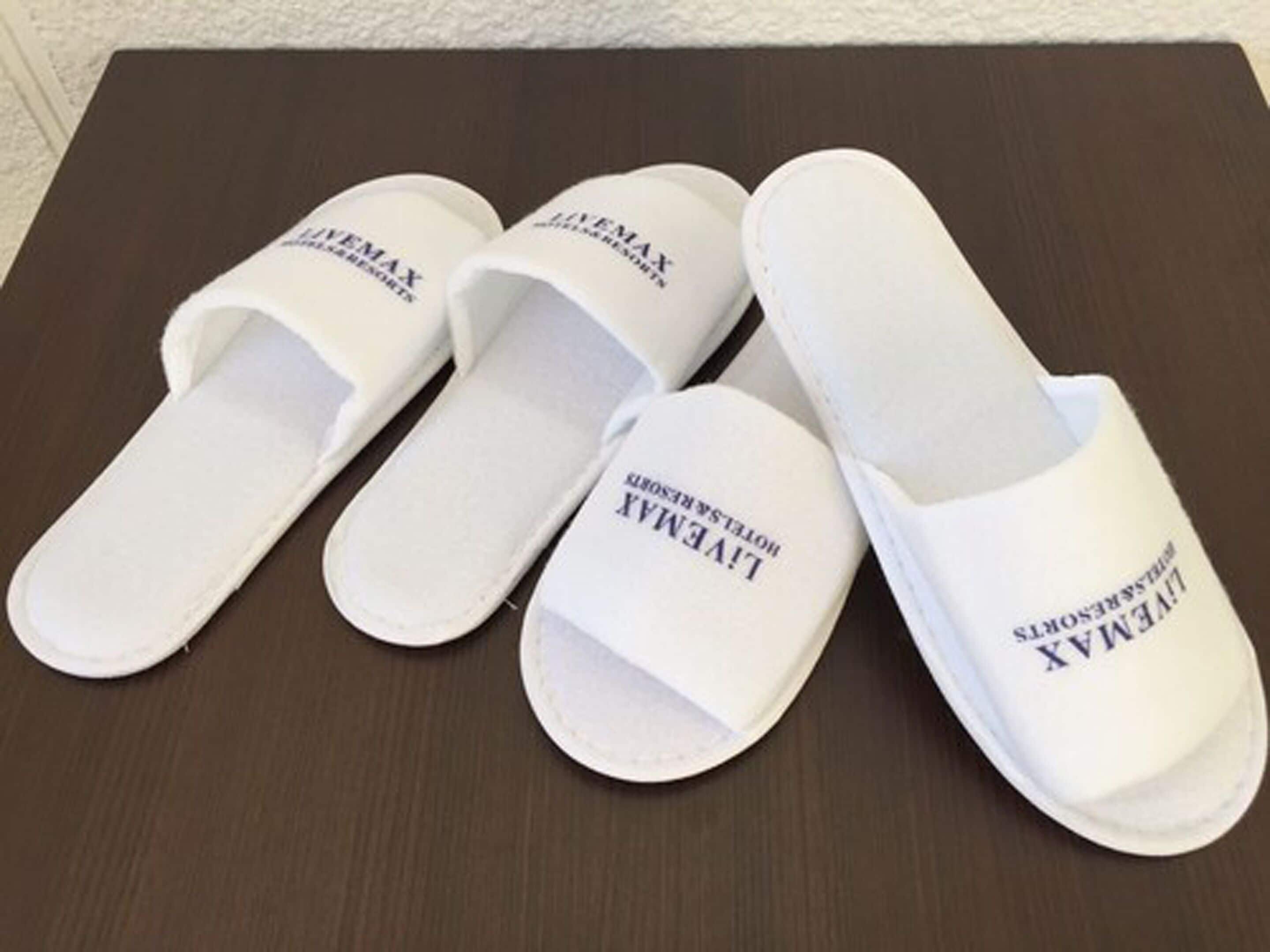Four white slippers with "LIVEMAX" printed on them, placed on a dark wooden surface.