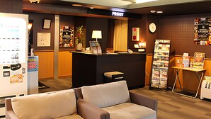 Un hall de hotel con mostrador de recepción, una zona de estar con dos sofás, un refrigerador y una cafetera.