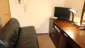 Una habitación con un sofá de cuero, un escritorio de madera con una computadora, una lámpara y un teléfono.