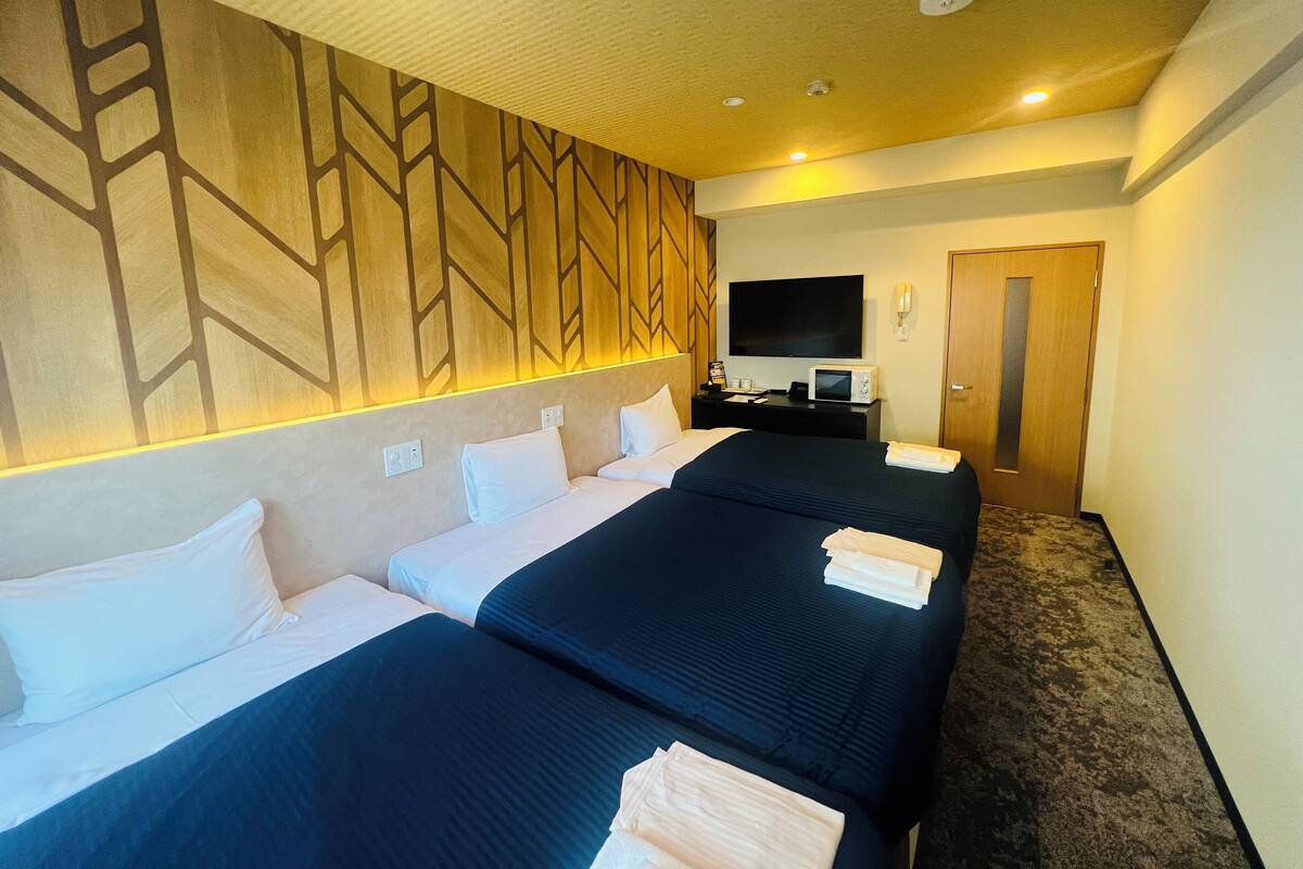 A hotel room with two beds, a flat-screen TV, a microwave, and a wooden accent wall.