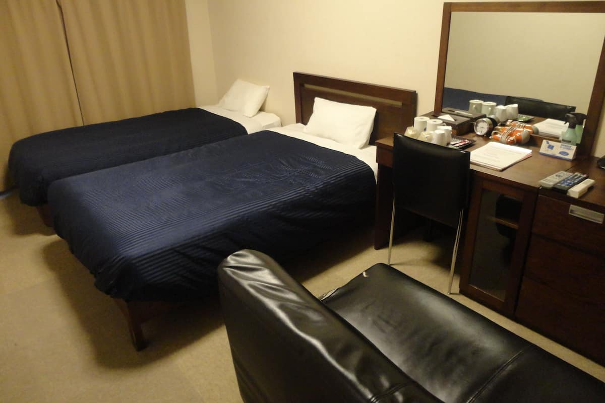 A hotel room with two beds, a desk, a chair, a mirror, and a small table with toiletries.