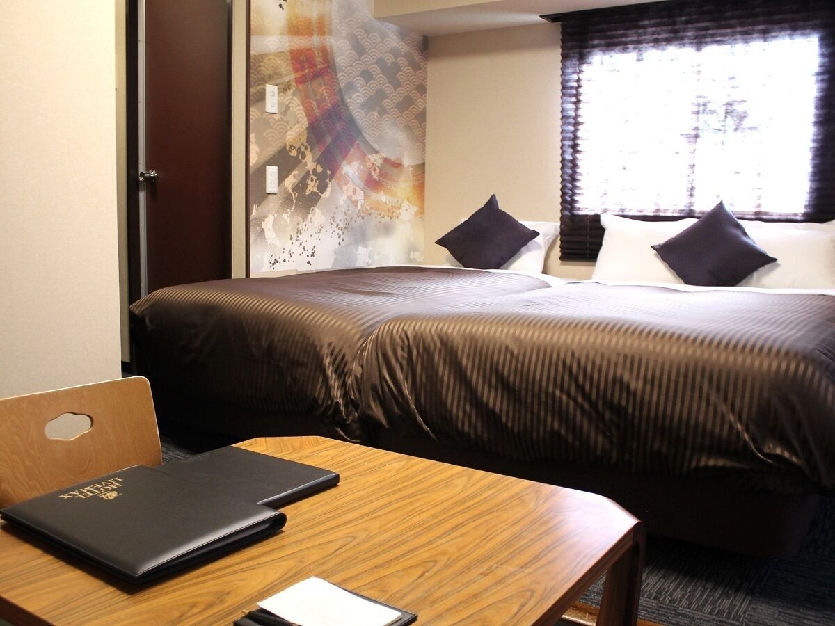 Een hotelkamer met een bed, een houten bureau met een laptop en een glazen scheidingswand.