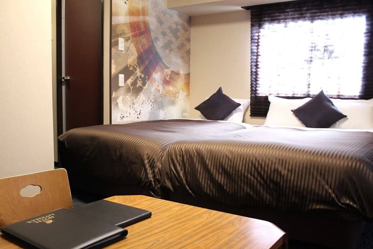 A hotel room with a bed, a wooden desk with a laptop, and a glass partition.