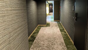 Un couloir aux murs sombres et à la texture marquée, un sol recouvert de moquette et une porte sur le côté droit.