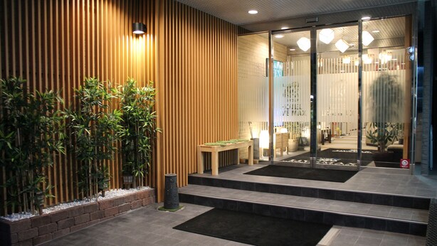 Une entrée moderne, avec un mur composé de lattes de bois, un banc et une porte en verre donnant accès à l’intérieur.