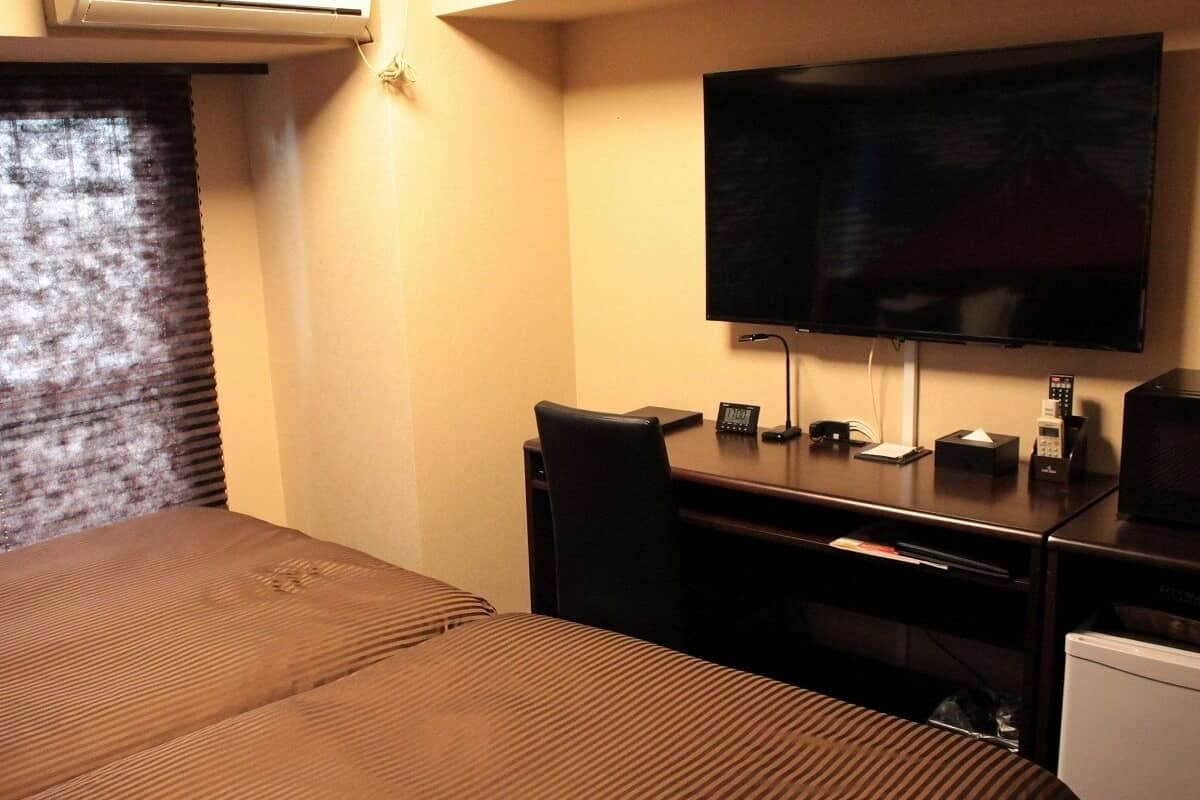 A hotel room with a bed, a desk, a television, and a small refrigerator.