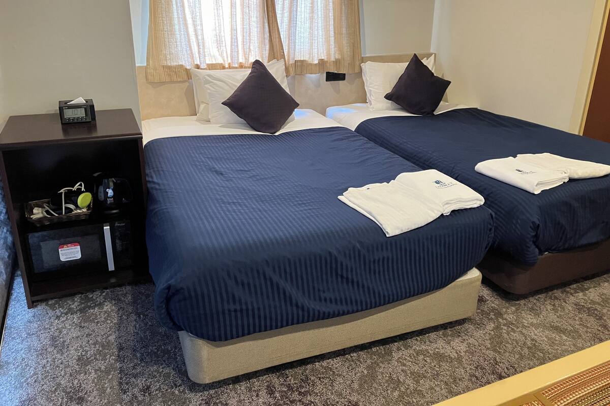 Une chambre d’hôtel avec deux lits, une table de chevet avec une horloge et une petite armoire contenant des articles de toilette.