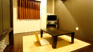 A room with a tatami mat, a dark wooden table, a television on a stand, and a window with brown curtains. - HOTEL LiVEMAX Esaka (Suita)
