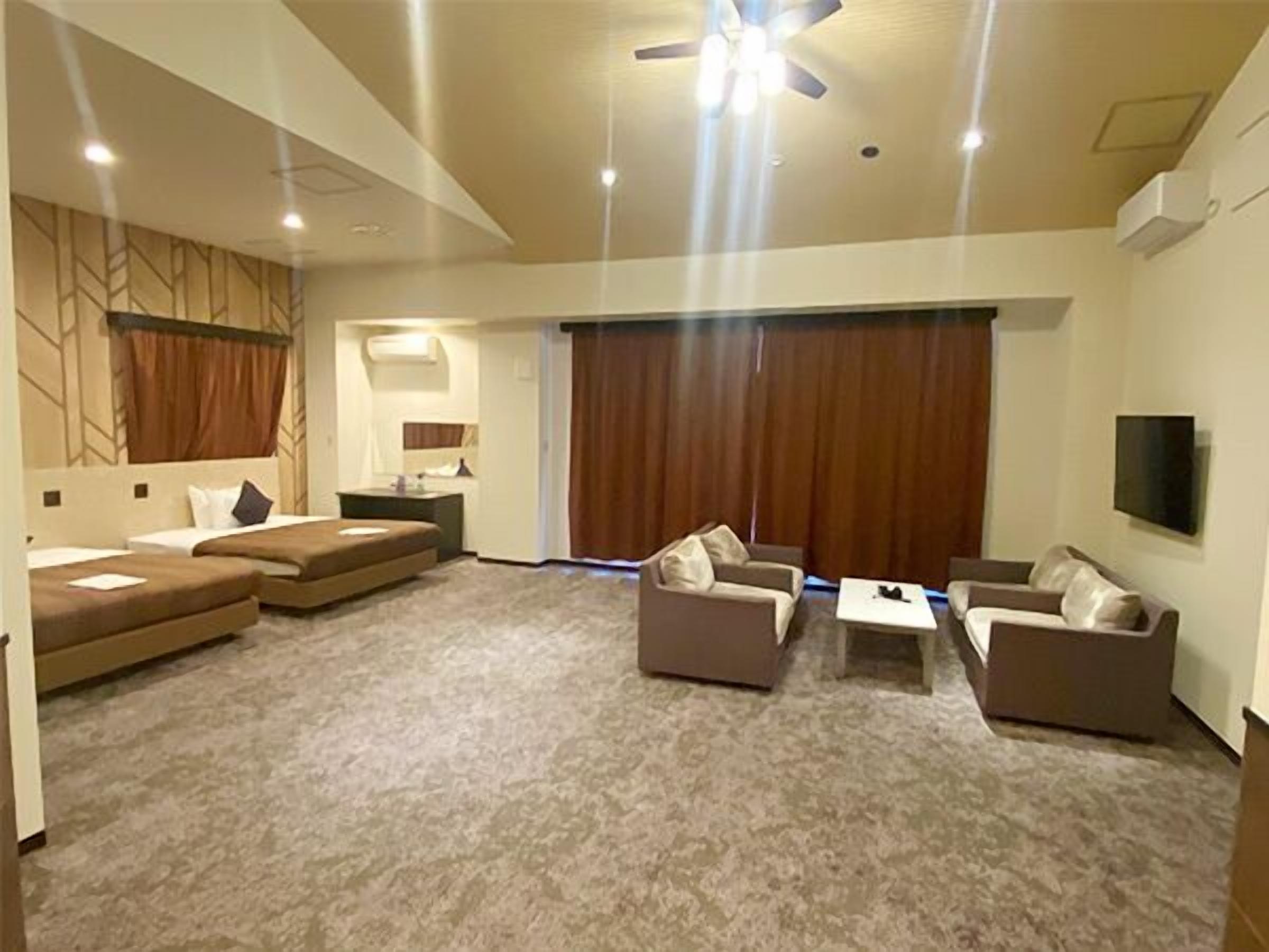 A hotel room with a large bed, a sofa, a coffee table, a TV, and a ceiling fan.