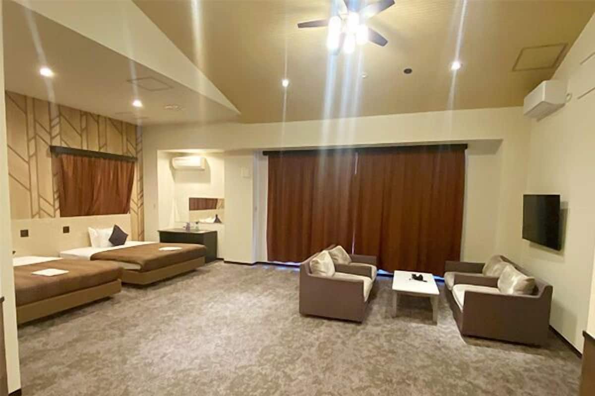 A hotel room with a large bed, a sofa, a coffee table, a TV, and a ceiling fan.