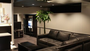 A modern living room with a leather sofa, a flat-screen TV, and a potted plant. - HOTEL LiVEMAX Esaka (Suita)