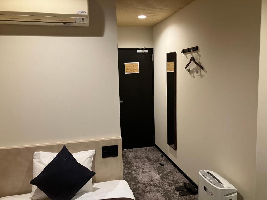 Quarto de hotel com cama, mesa de cabeceira, espelho, porta-roupas e ar condicionado fixado na parede.