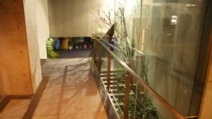 A corridor with a tiled floor, a glass railing, and a staircase with a metal railing.