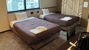 A hotel room with two beds, a desk, and a view of the city through large windows.