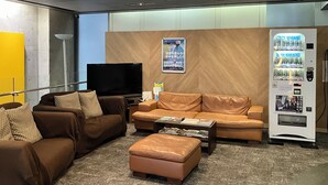 A modern living room with leather sofas, a flat-screen TV, a vending machine, and a poster on the wall.
