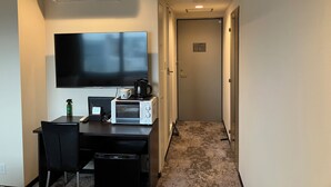 A compact hotel room with a kitchenette, a flat-screen TV, a coffee maker, and a microwave.