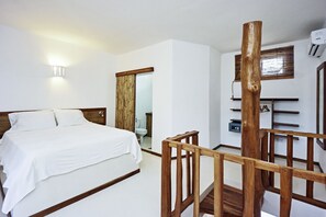 A bedroom with a bed, wooden headboard, a mirror, a wooden railing, and a shelf with a small item on it. - Otro Lado Lodge and Restaurant (Cobano)
