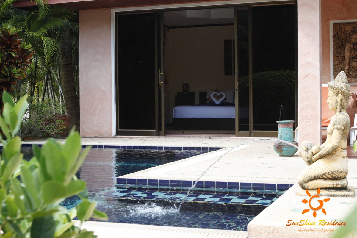 A pool area with a statue, a bed visible through a sliding door, and a heart-shaped decoration on the bed.