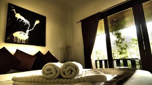 A hotel room with a bed, a painting on the wall, and a view of greenery through the window. - Cocooning Hotel (Koh Samui)