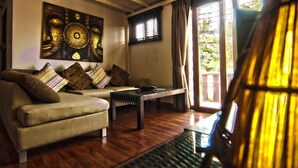A living room with a sofa, a coffee table, and a large Buddha painting on the wall. - Cocooning Hotel (Koh Samui)