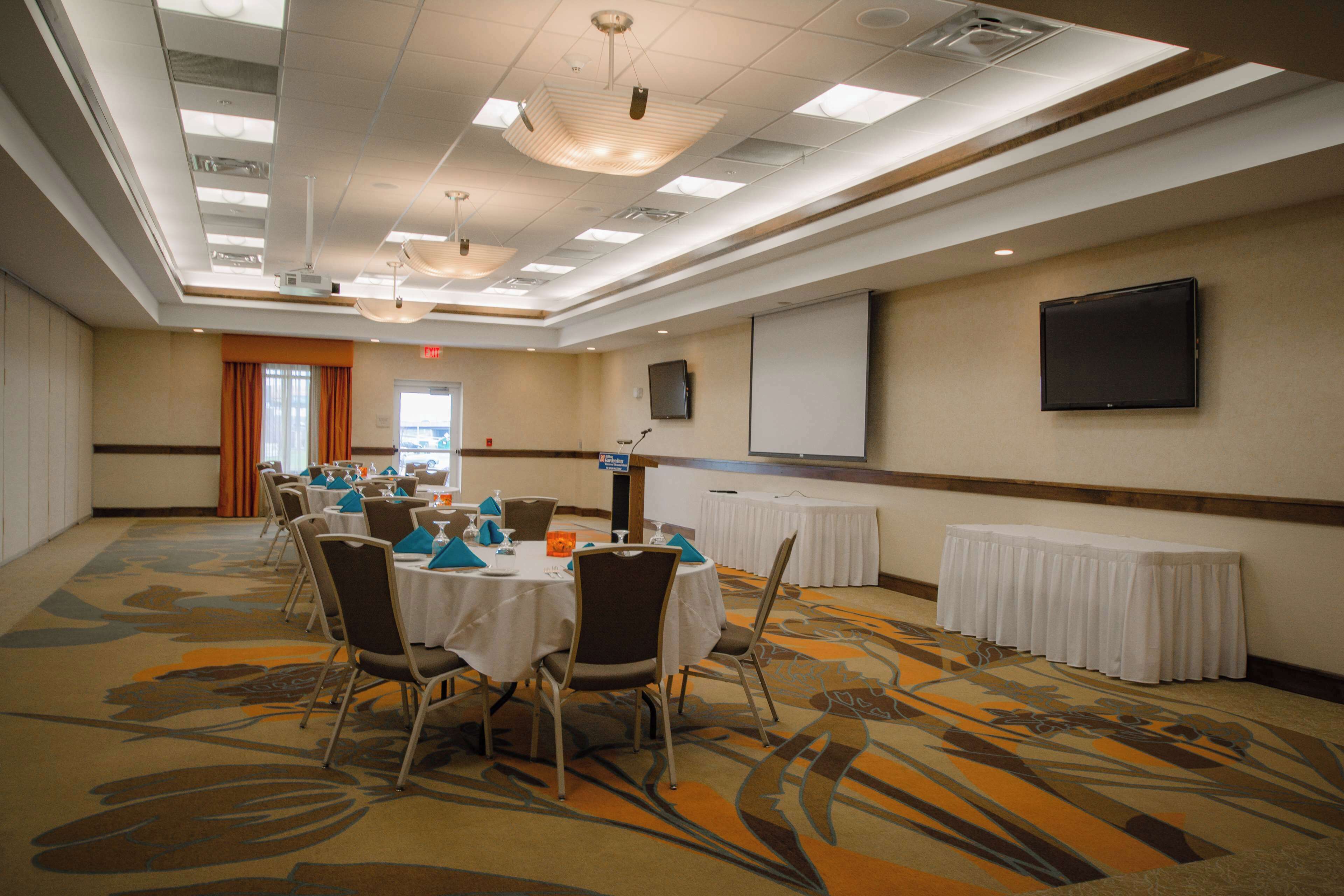 A conference room with round tables, chairs, a projector screen, and a television on the wall.