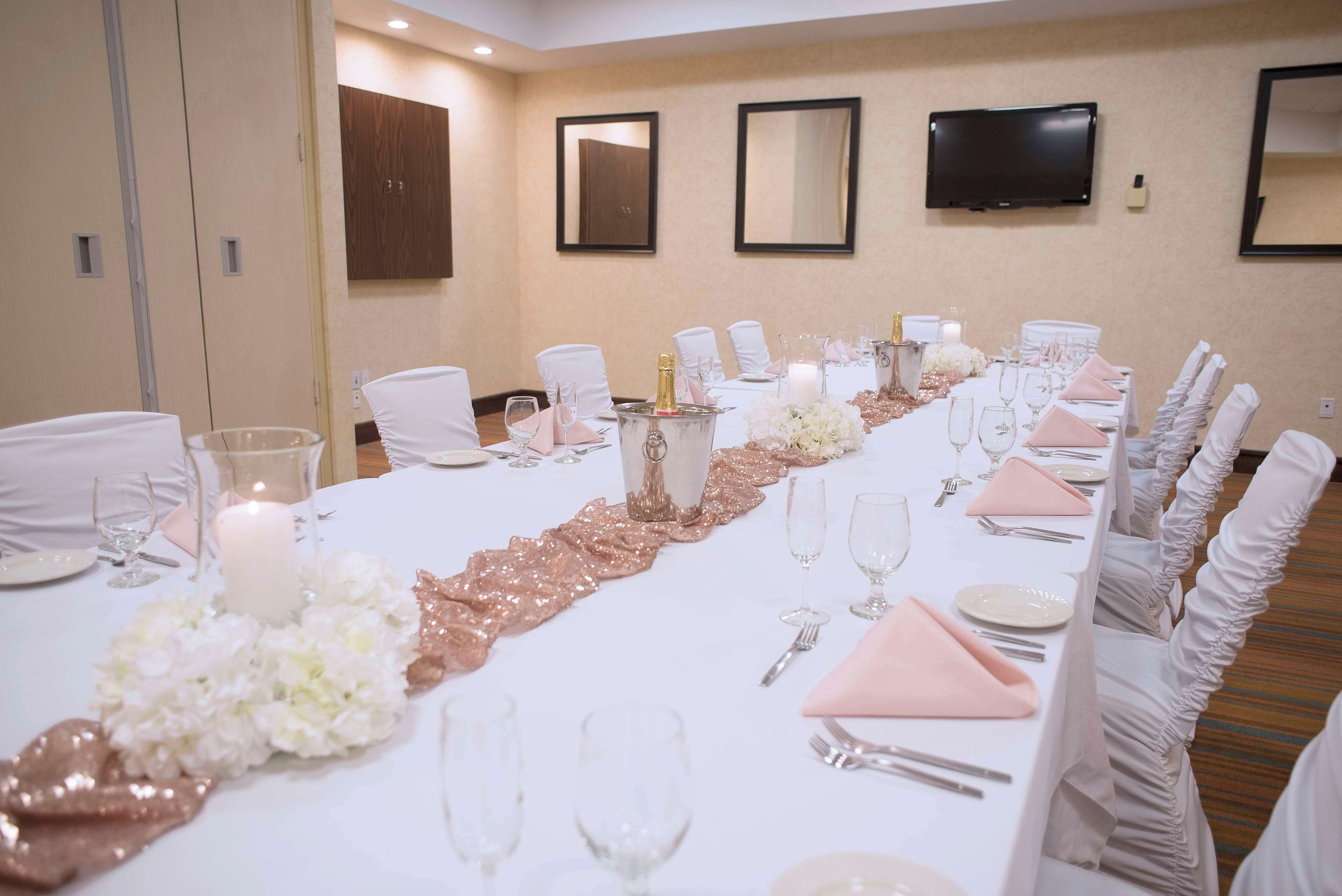 A long banquet table set with white tablecloths, pink napkins, and white chairs.