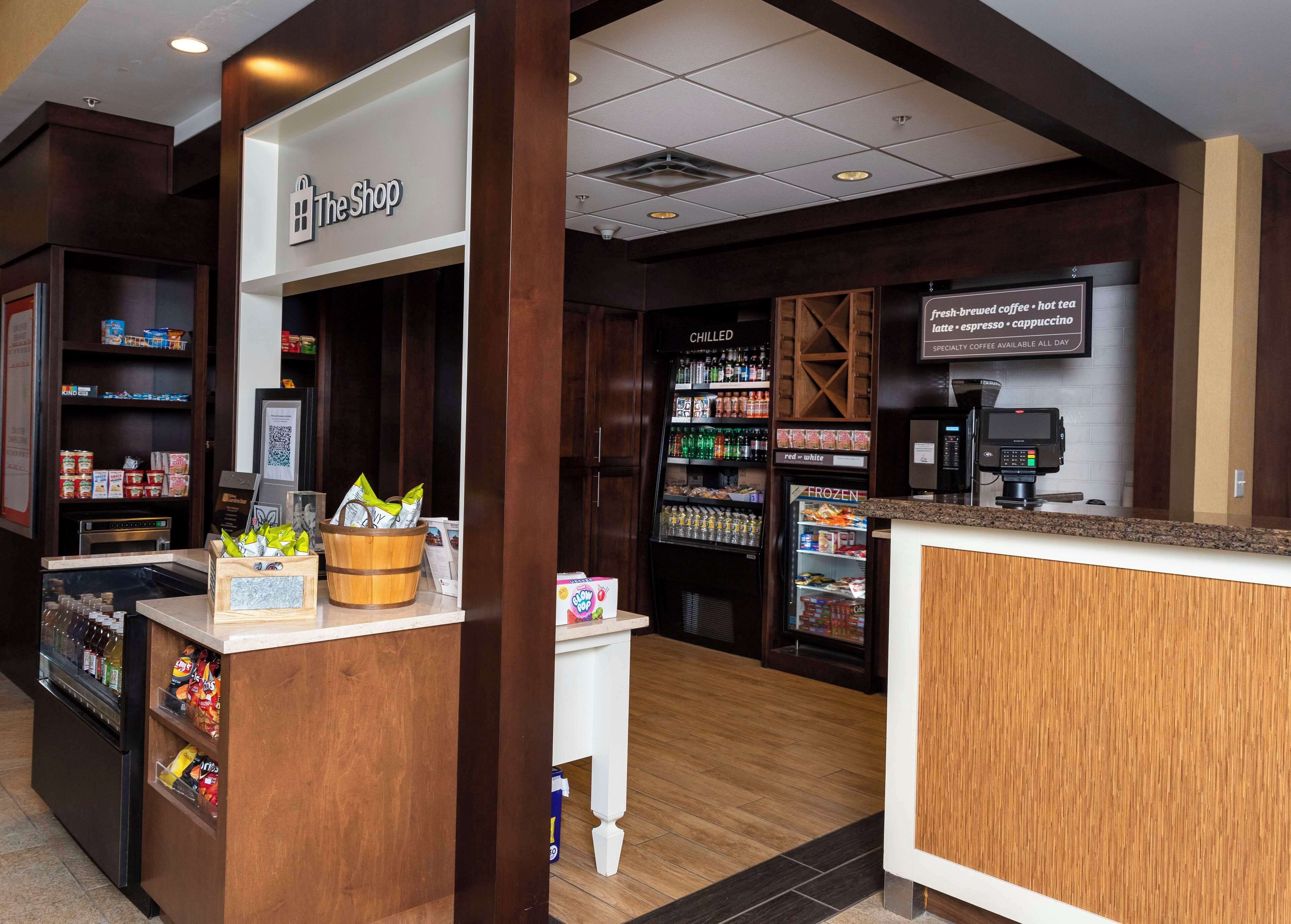 L’intérieur d’un café, avec un comptoir, un présentoir réfrigéré pour les boissons et une enseigne indiquant « The Shop ».