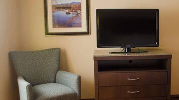 A room with a framed landscape painting, a television on a wooden stand, a patterned armchair, and a carpeted floor.