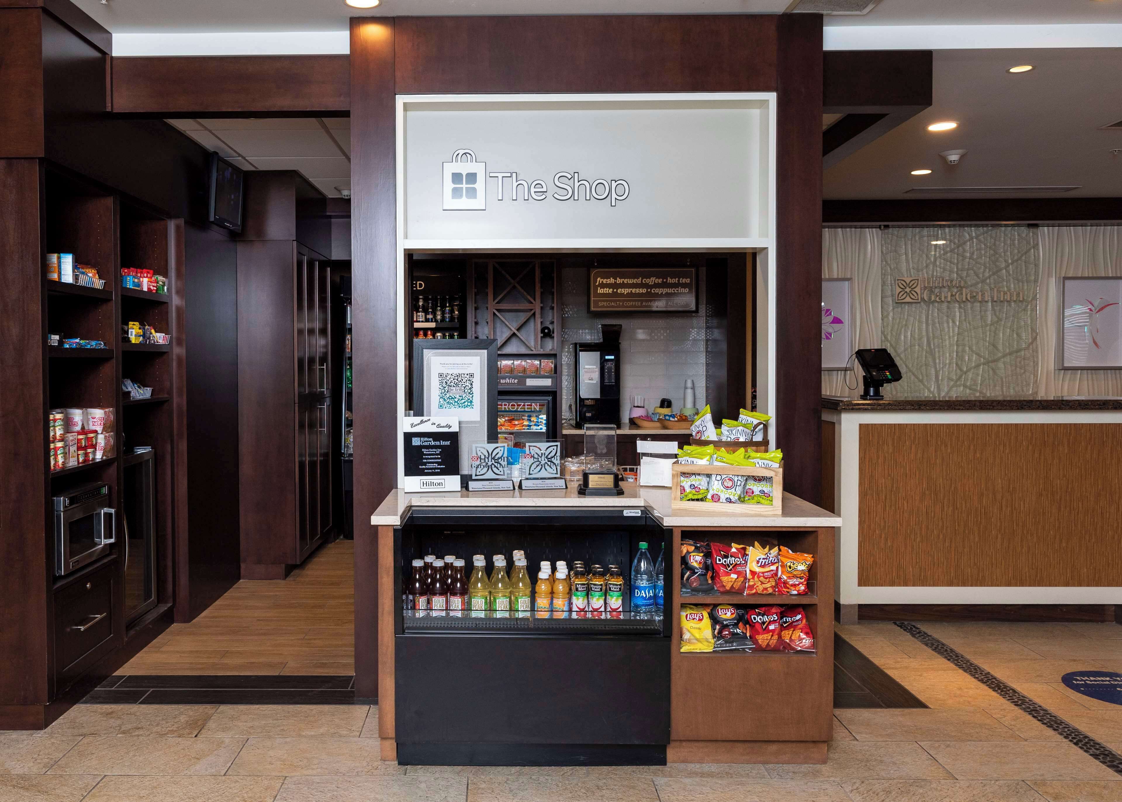 Un vestíbulo de hotel con un quiosco de autoservicio identificado como “The Shop”, que ofrece bebidas y aperitivos.