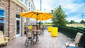 An outdoor patio with tables and chairs, a yellow umbrella, and a stone building.
