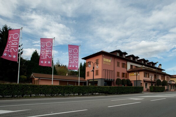 A hotel with a pink facade, multiple flags, and a clear sky. - Sirio Hotel (Dormelletto)